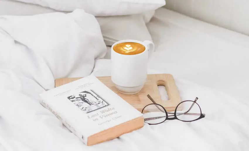 cup of coffee with a book on a bed